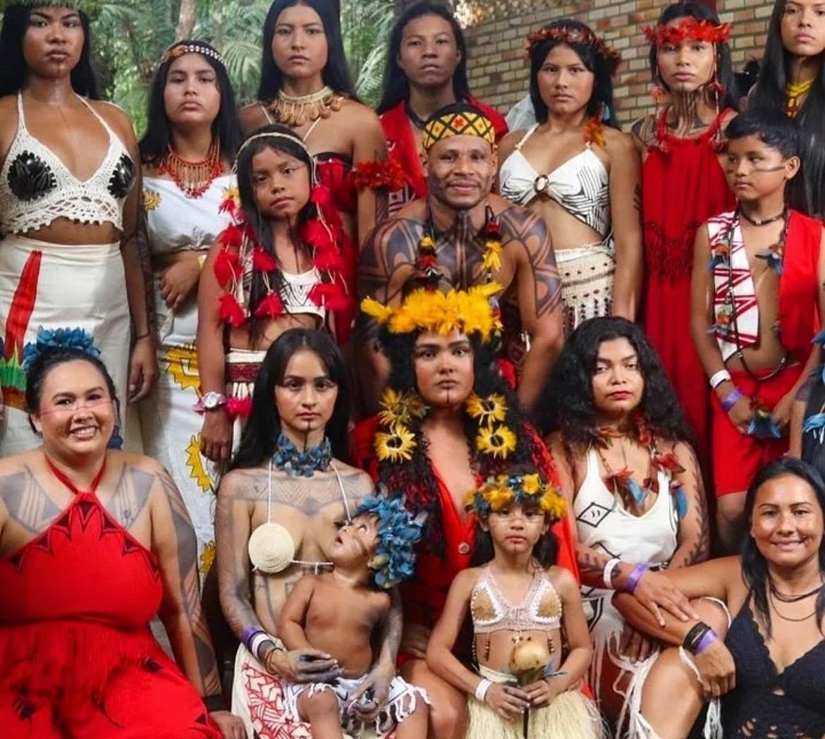 Grupo de mulheres, homens e crianças indígenas com trajes, cocares e pinturas tradicionais